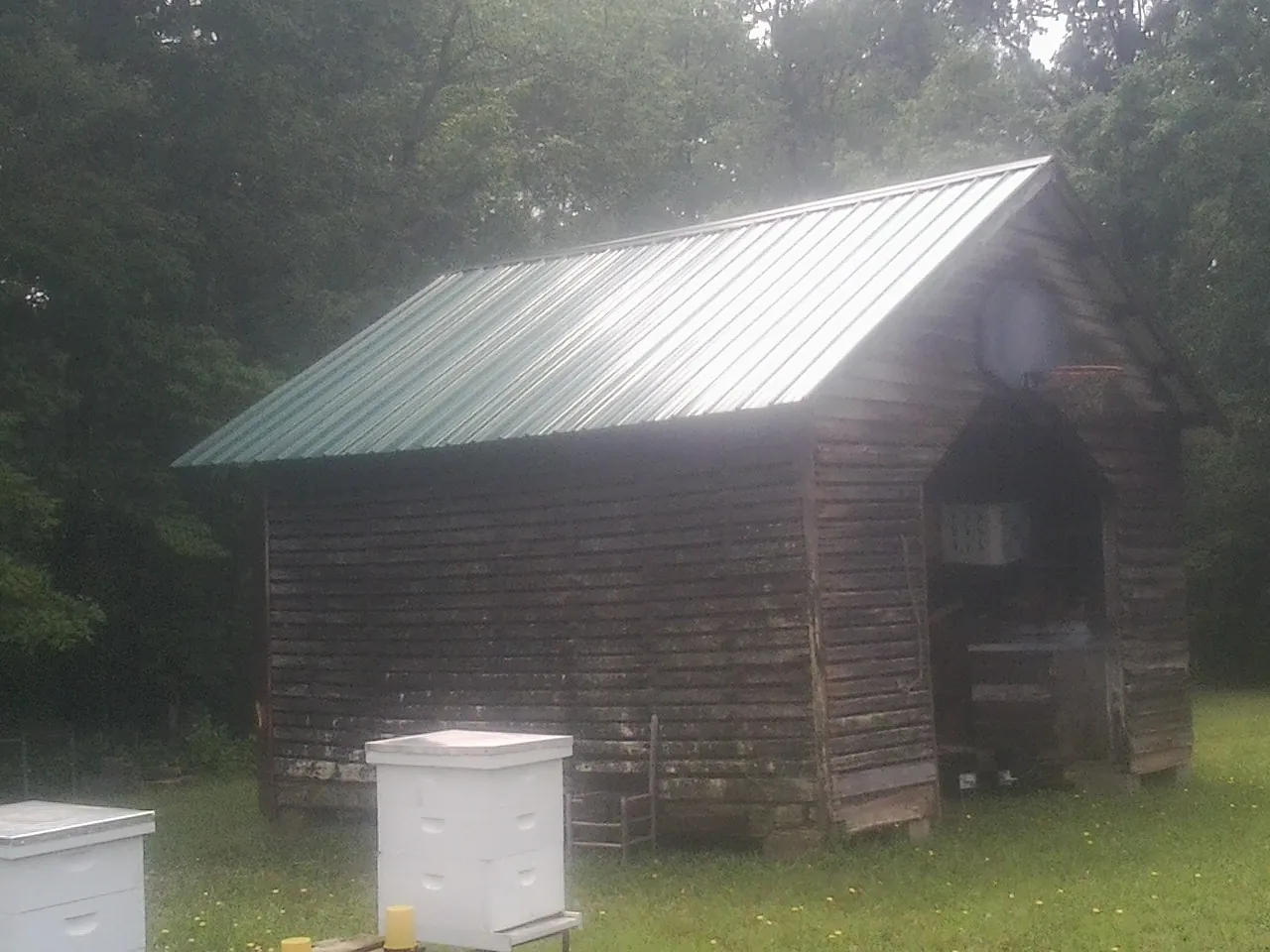 Green metal roof on a weathered barn beside stacked beehives in Rutland