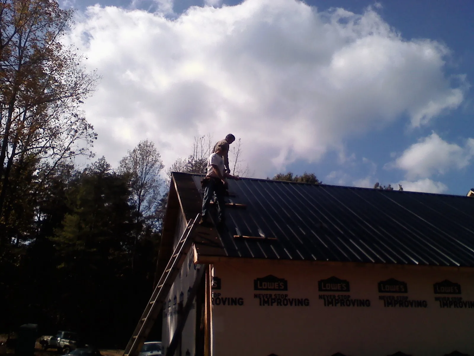 Roofer fastening dark metal panels high against a cloudy sky, from a Roof Inspection job in Rutland